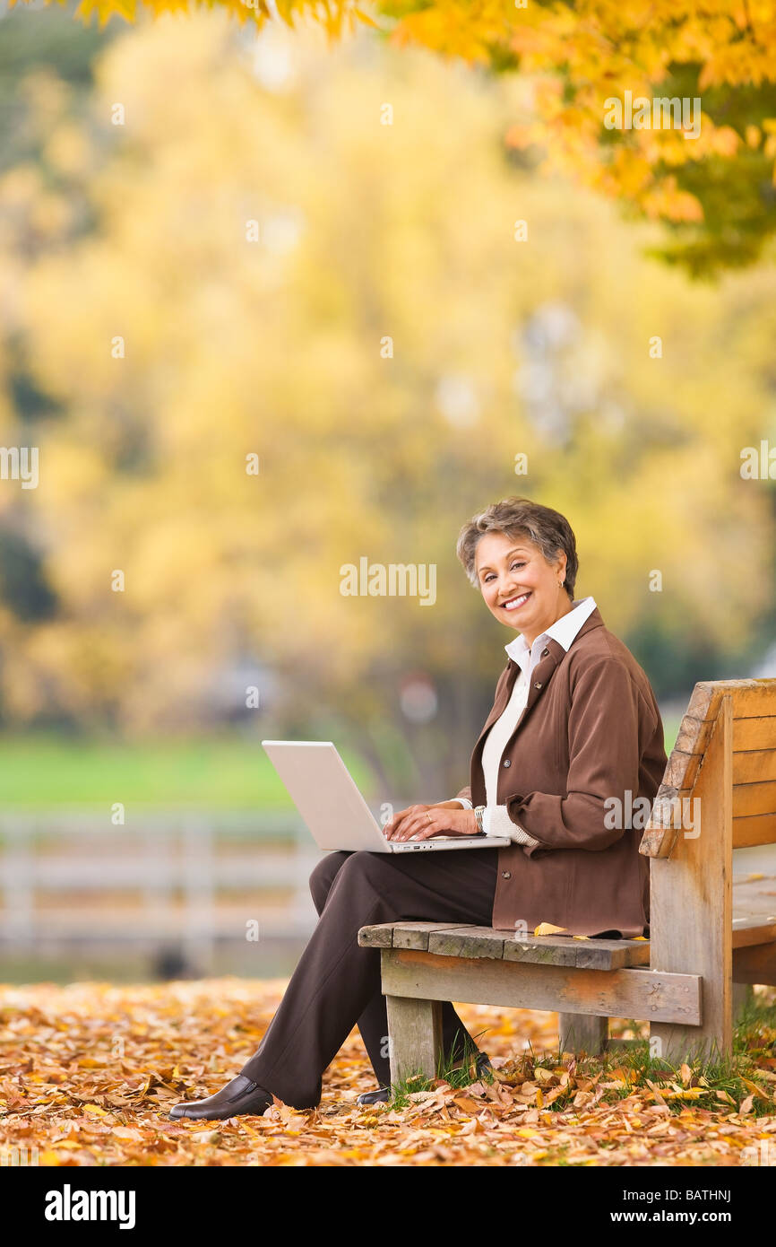 Donna africana utilizzando portatile su una panchina nel parco in autunno Foto Stock