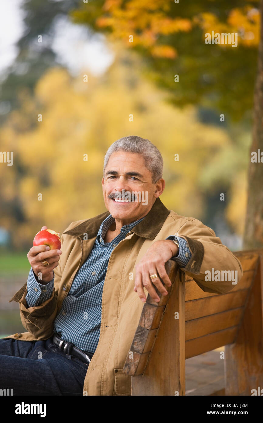L'uomo africano mangiare apple su una panchina nel parco Foto Stock