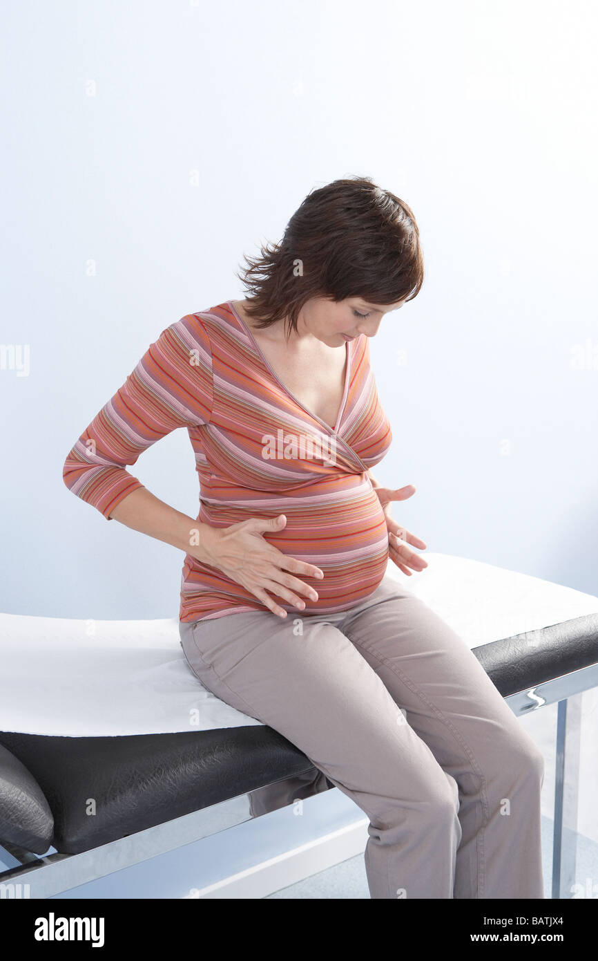 Donna incinta seduta su un lettino, in attesa di una consultazione. Foto Stock