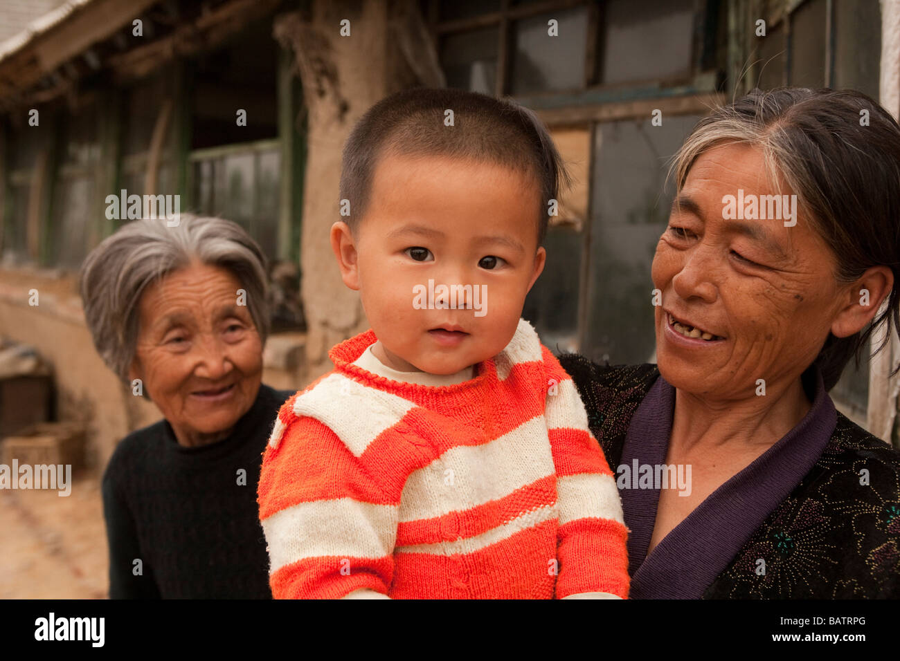 Changchun, provincia di Jilin, Cina. Un giovane ragazzo tra le braccia della madre al di fuori della loro casa con la sua nonna dietro. Foto Stock