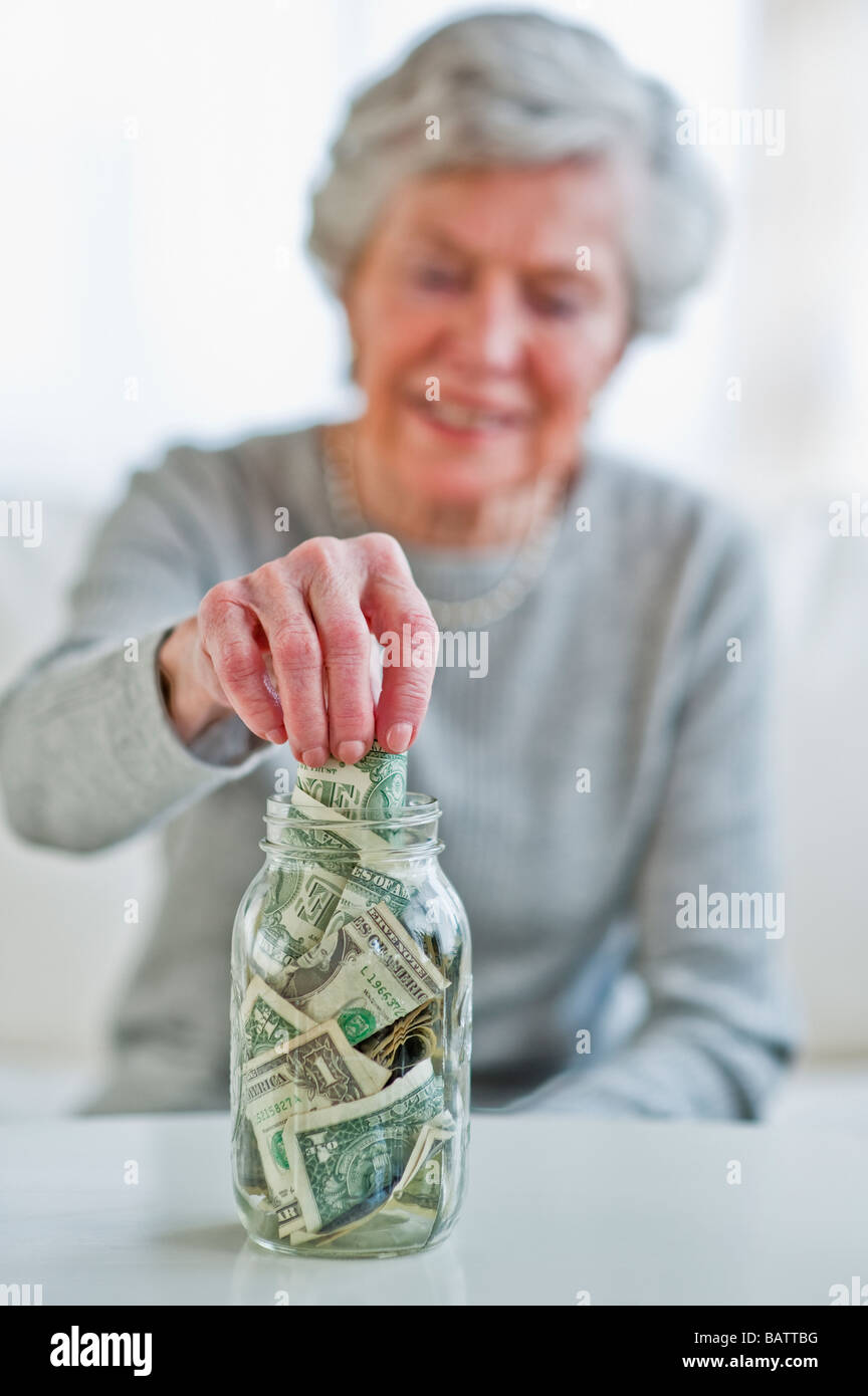 Senior donna mettendo la banconota in denaro jar Foto Stock