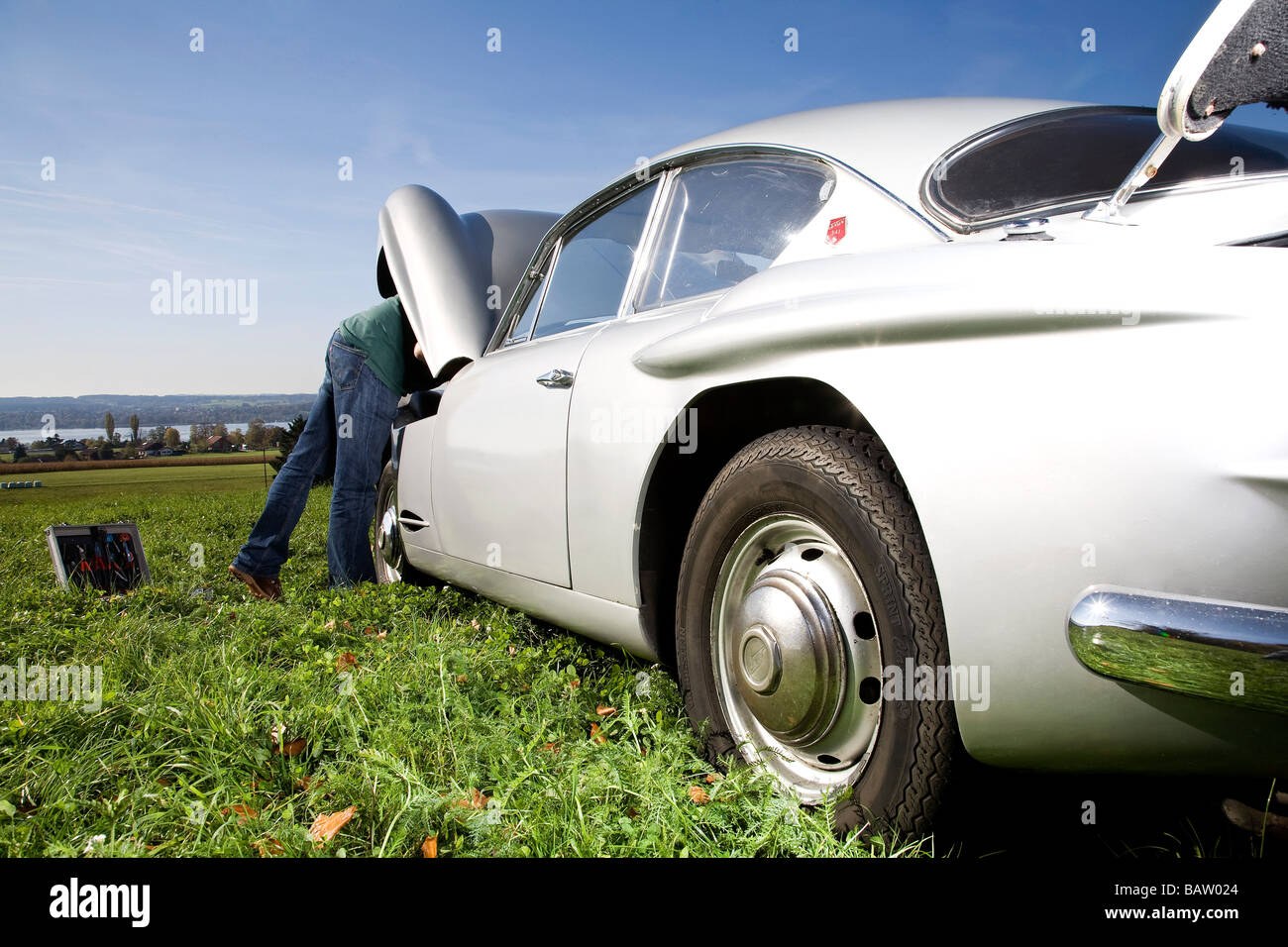 Uomo che ripara il suo classico auto sul prato Foto Stock