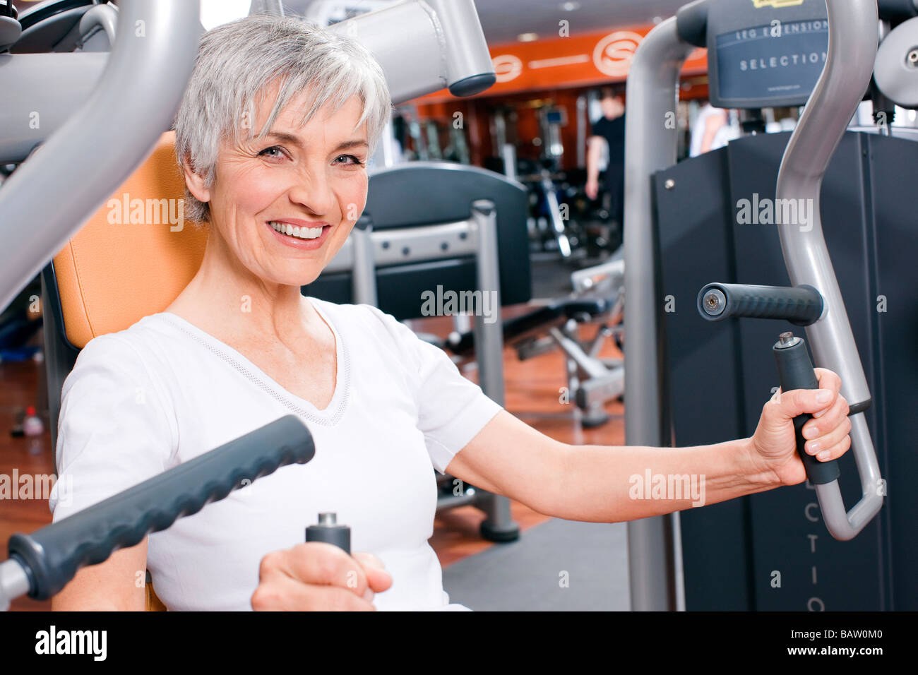 Donna matura che esercitano sulla macchina per pesi nella palestra Foto Stock