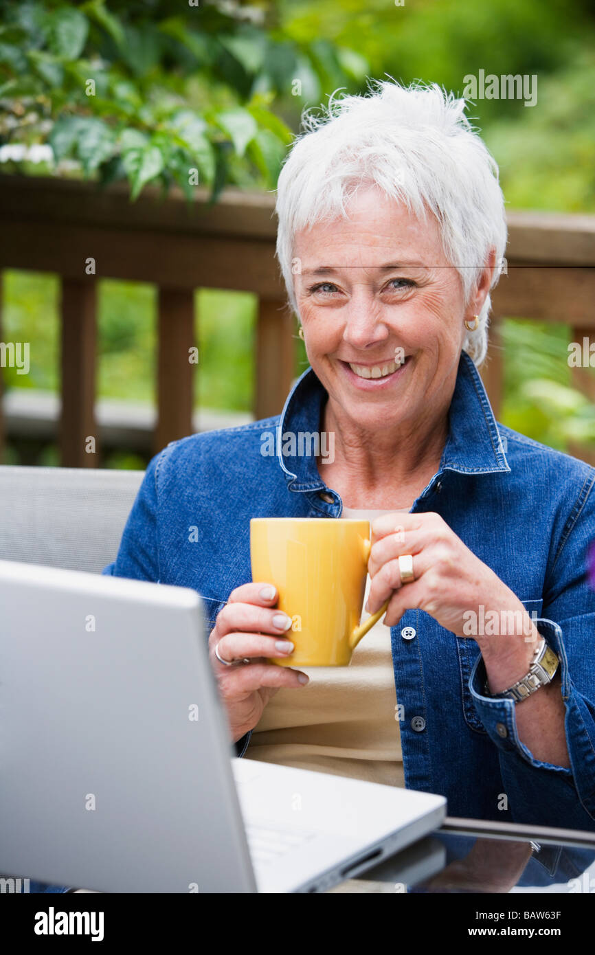 Senior donna con caffè e laptop all'aperto Foto Stock