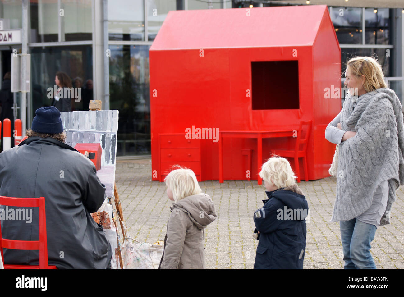 L'artista di strada seduta pittura capanna rosso curiosi i bambini madre famiglia guardare, Rotterdam Paesi Bassi Foto Stock
