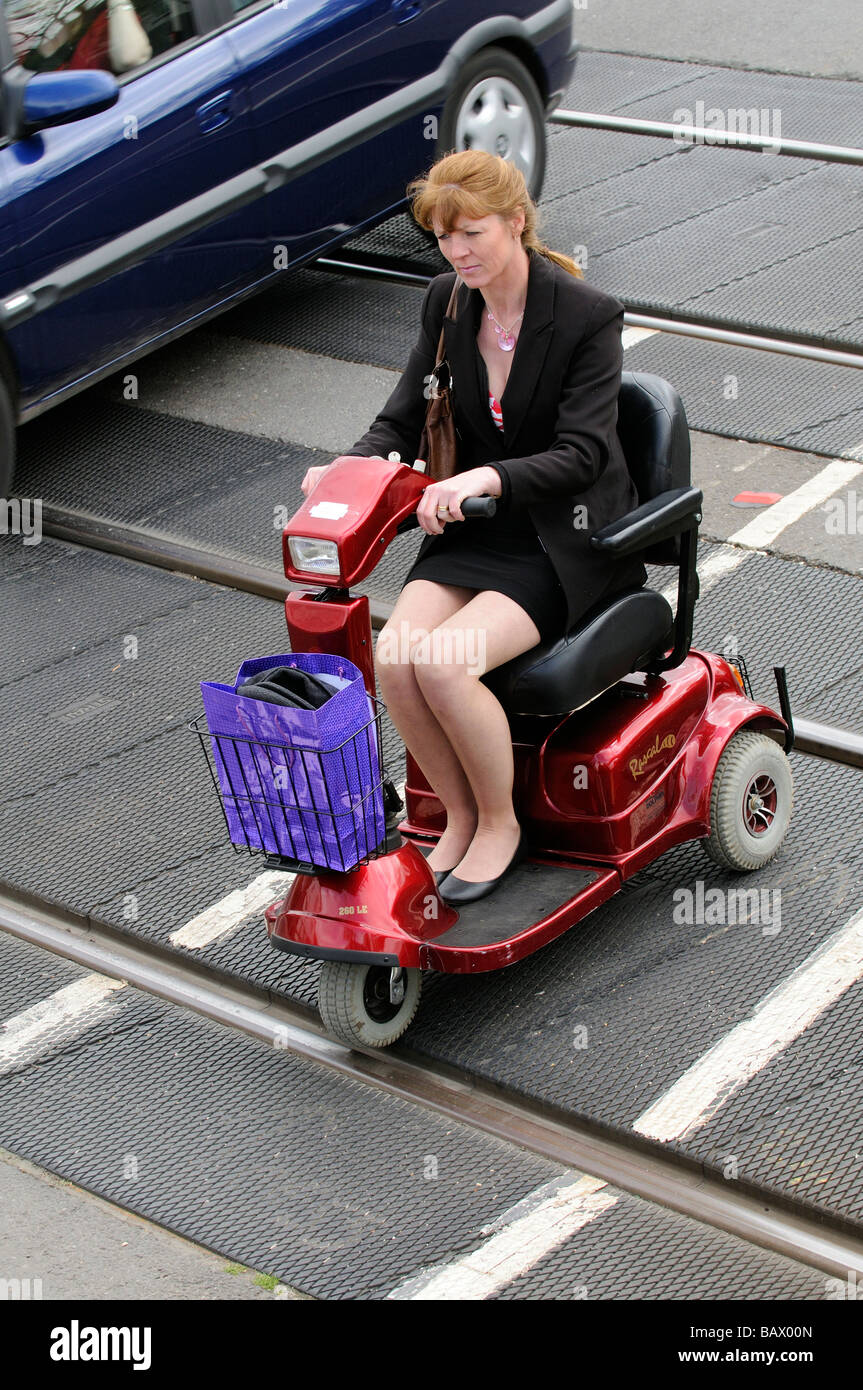 Donna alla guida del suo scooter di mobilità attraverso un passaggio a livello ferroviario percorso England Regno Unito Foto Stock