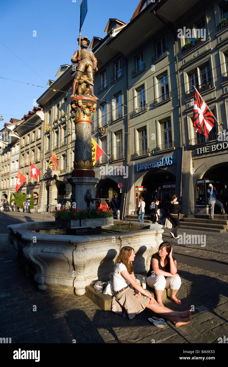 Due giovani donne ubicazione davanti ad una fontana, Schuetzenbrunnen, Marktgasse, la città vecchia di Berna, Berna, Svizzera Foto Stock