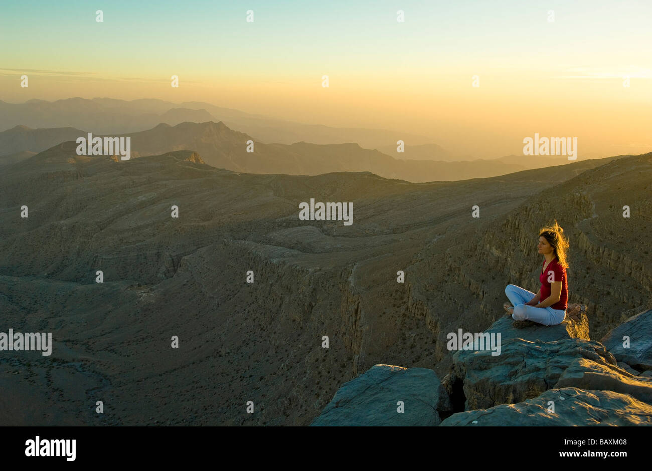 Donna seduta sul bordo di una roccia a guardare il tramonto, Sayh altopiano, paesaggio di montagna, Hajjar Monti, Kashab, Khasab, Mus Foto Stock