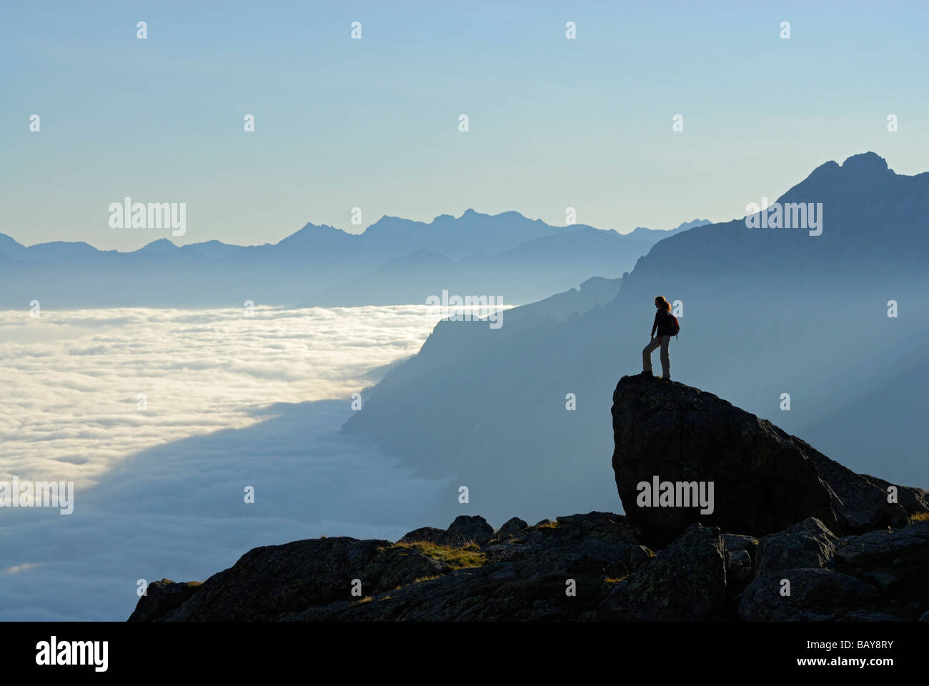Escursionista sulla rupe sopra banco di nebbia in Valle Gschnitztal, Bremer Huette, Stubaier Alpen gamma, Stubai, Tirolo, Austria Foto Stock