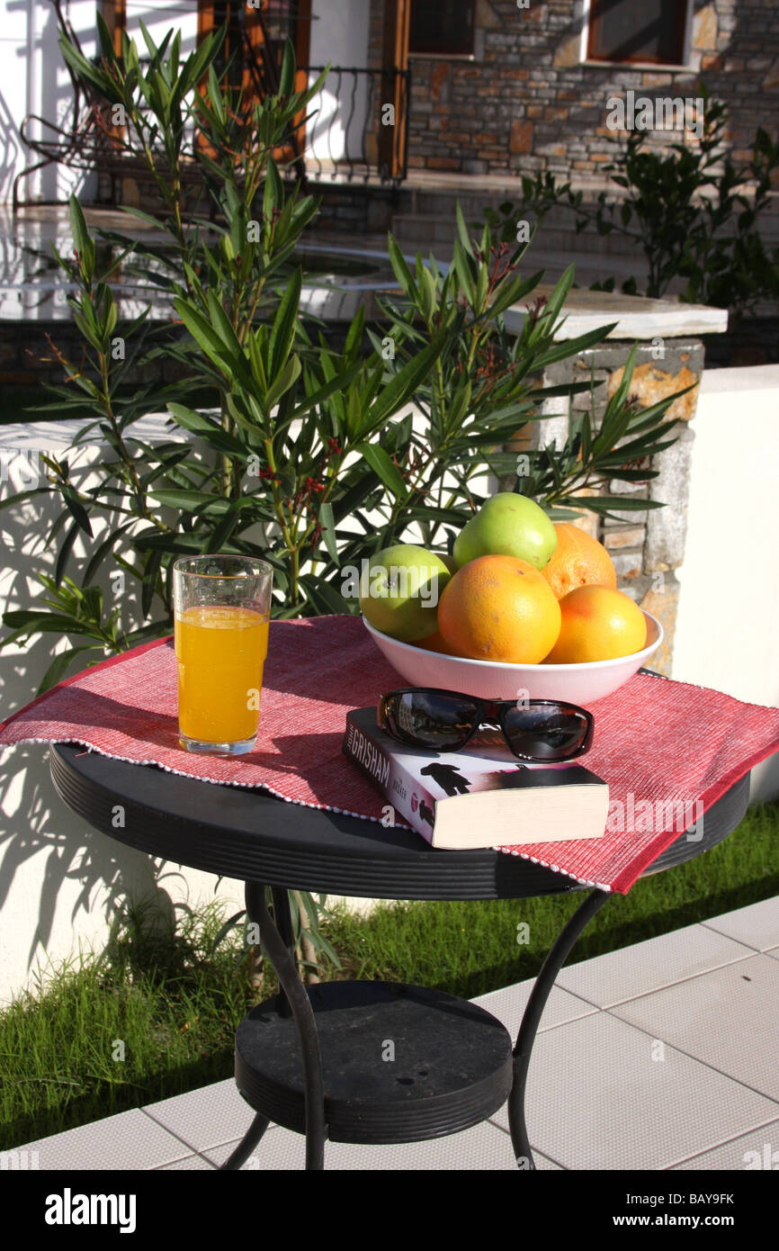 Tavolino rotondo con una ciotola di frutta, succo di arancia e un libro in brossura Foto Stock