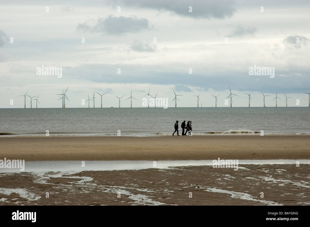 La gente che camminava su un freddo Skegness Beach con le centrali eoliche offshore in background Foto Stock