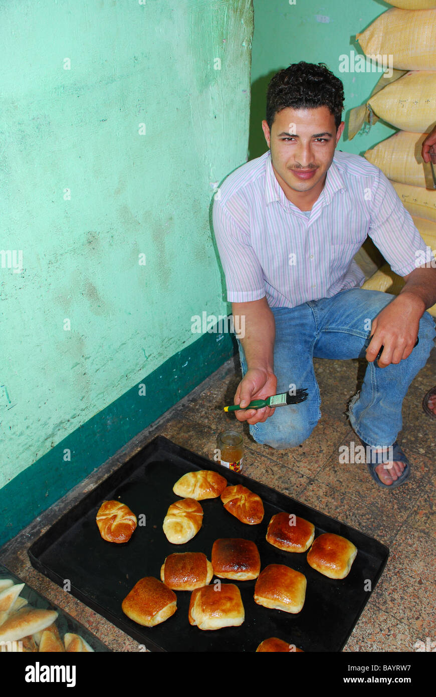 Giovane uomo egiziano di mettere lo zucchero smalto su pane a Luxor, Egitto Foto Stock