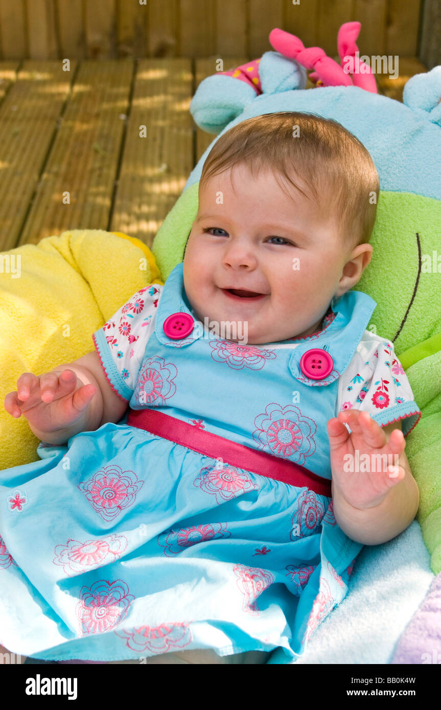 Chiudere verticale su ritratto di un simpatico sei mesi Baby girl ridere e scherzare nel giardino in una giornata di sole Foto Stock