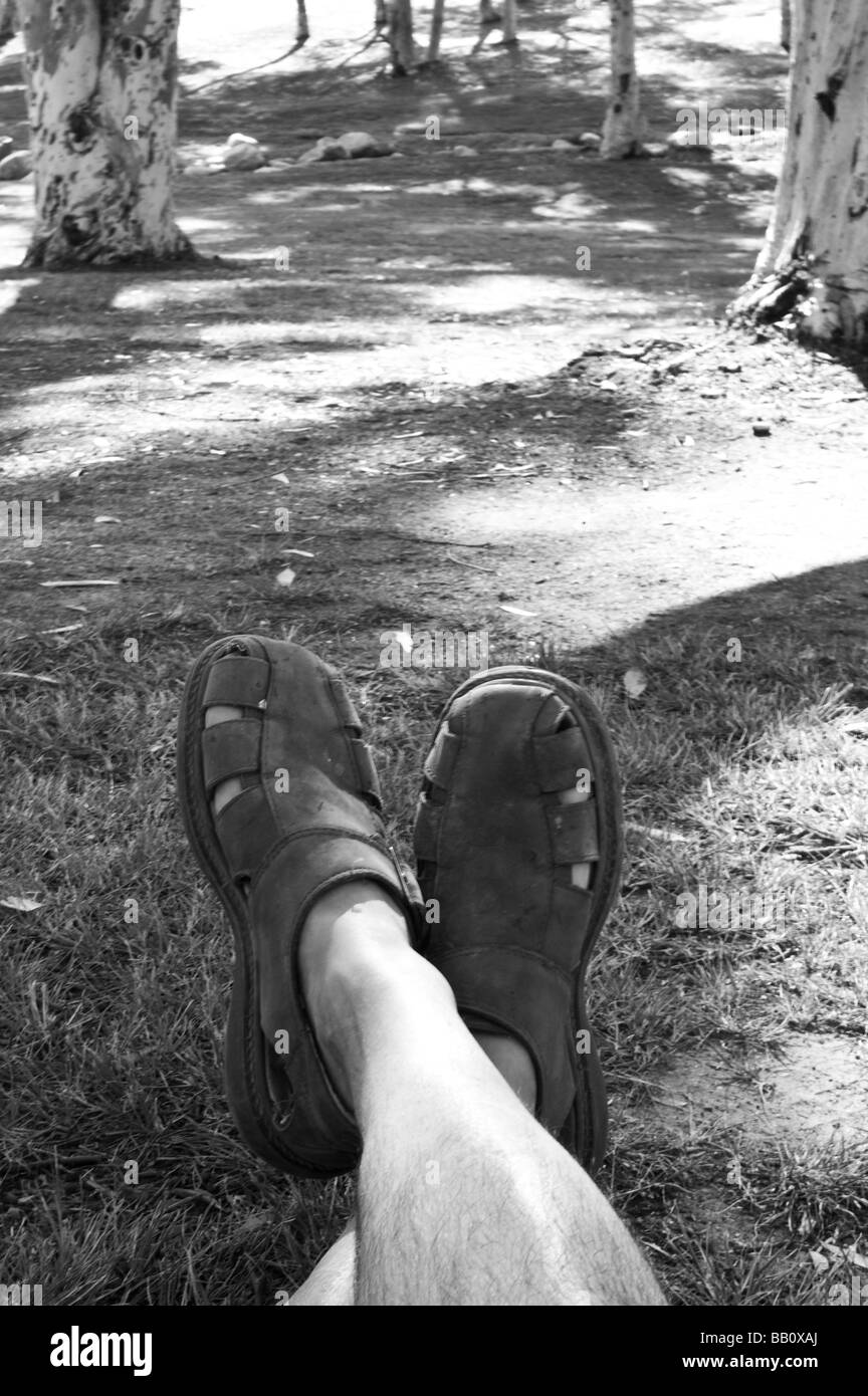 Un uomo che stabilisce in un parco a fotografare le sue gambe, con alberi in background Foto Stock