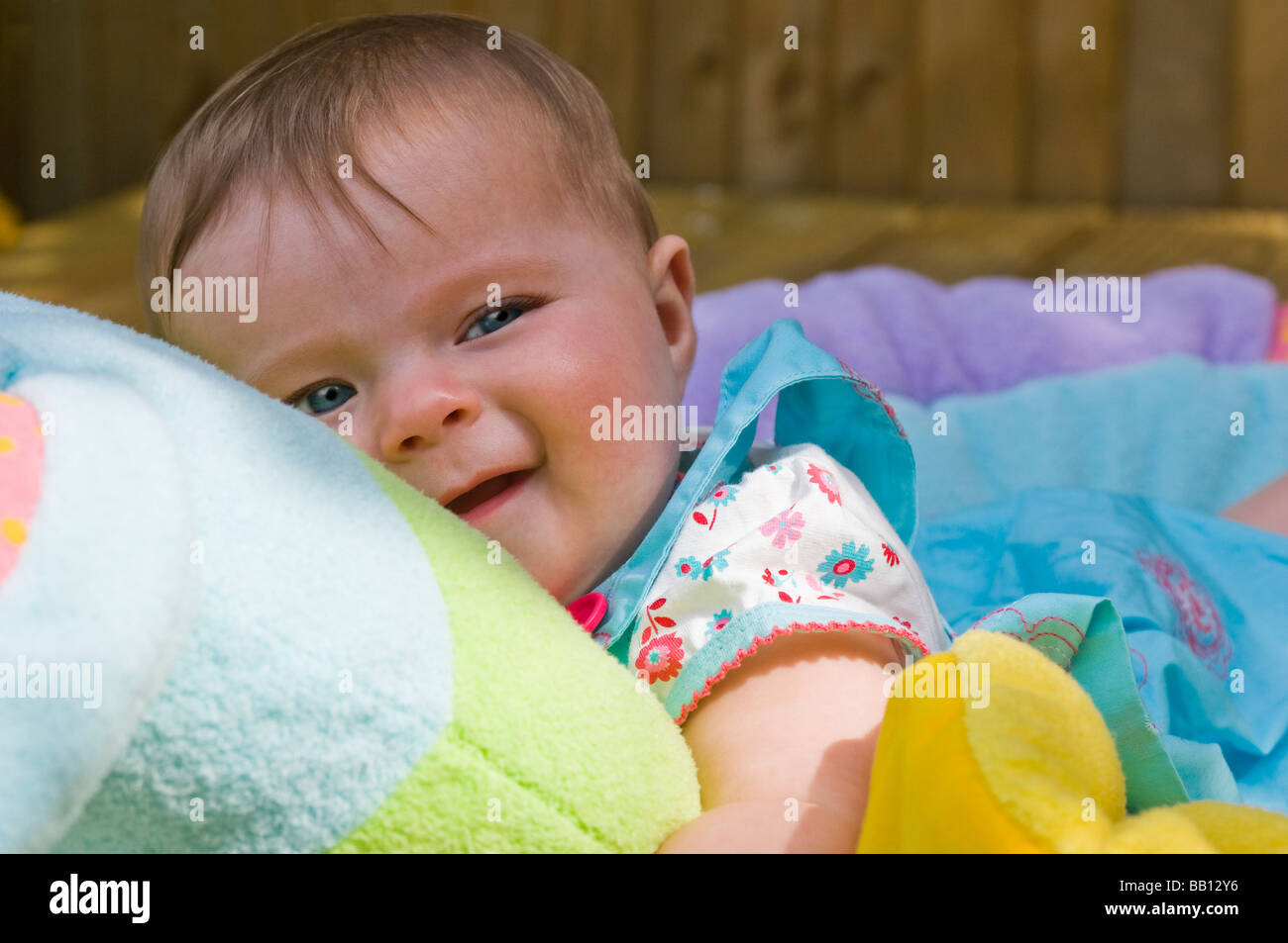 Chiudere orizzontale su ritratto di un simpatico sei mesi baby ragazza distesa su un cuscino colorato nel giardino in una giornata di sole Foto Stock