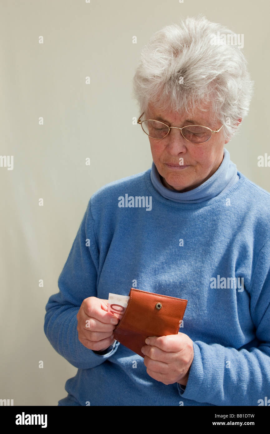 British senior donna che indossa un ponticello blu prendendo un dieci euro nota da un portafoglio cercando in questione. Europa Foto Stock