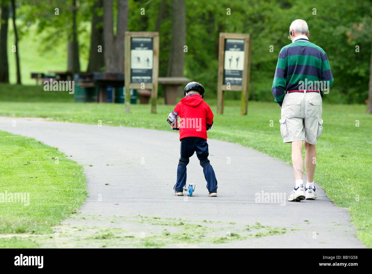 Un giovane ragazzo in sella alla sua razor kick scooter nel parco con è nonno. Foto Stock
