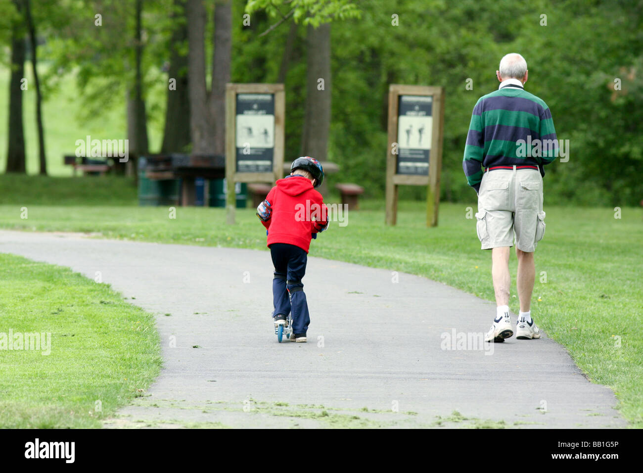 Un giovane ragazzo in sella alla sua razor kick scooter nel parco con è nonno. Foto Stock