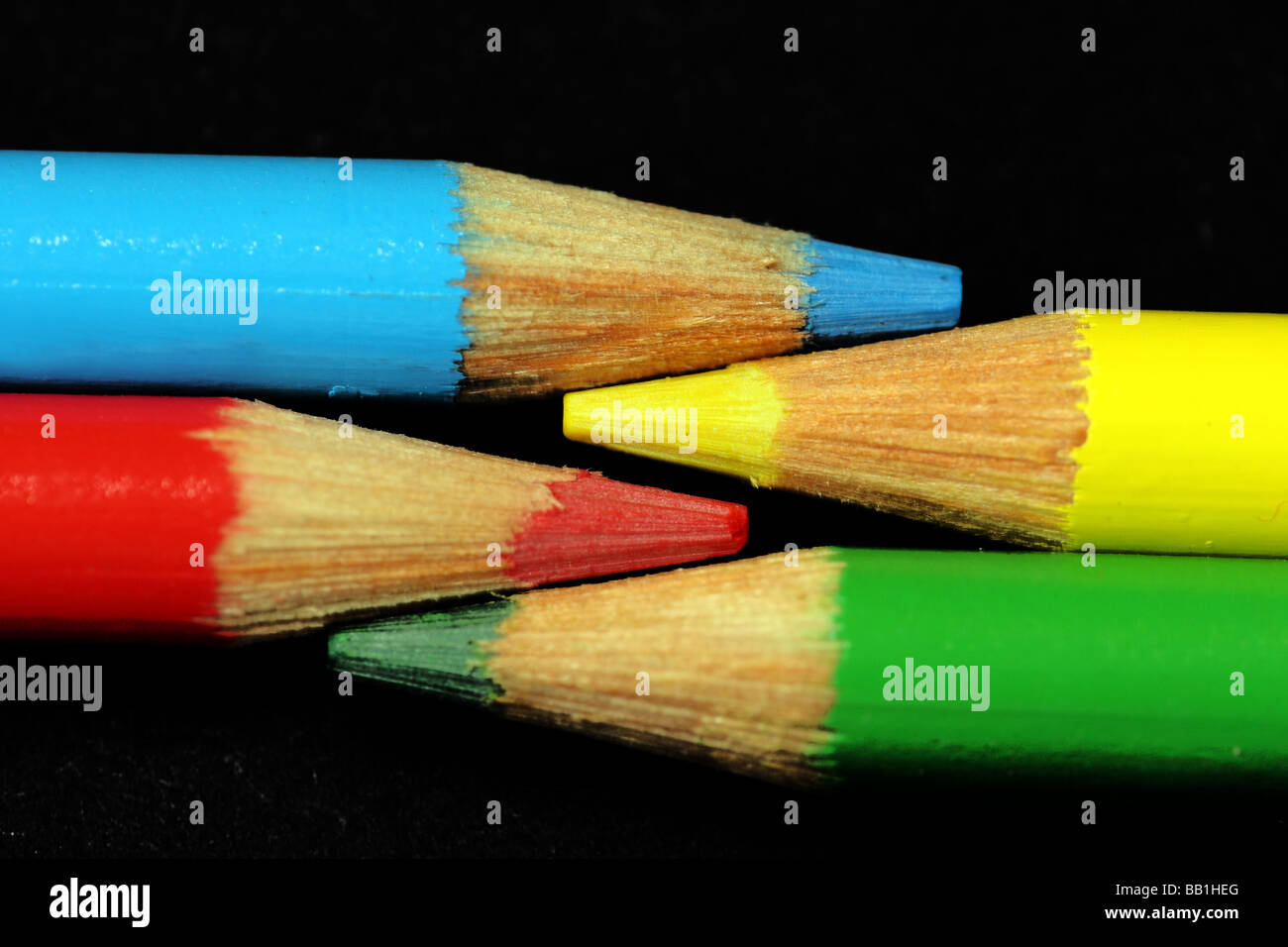 Vista macro di quattro matite colorate a fianco a fianco, Blu, Giallo, rosso e verde, punti affilati, su sfondo nero Foto Stock