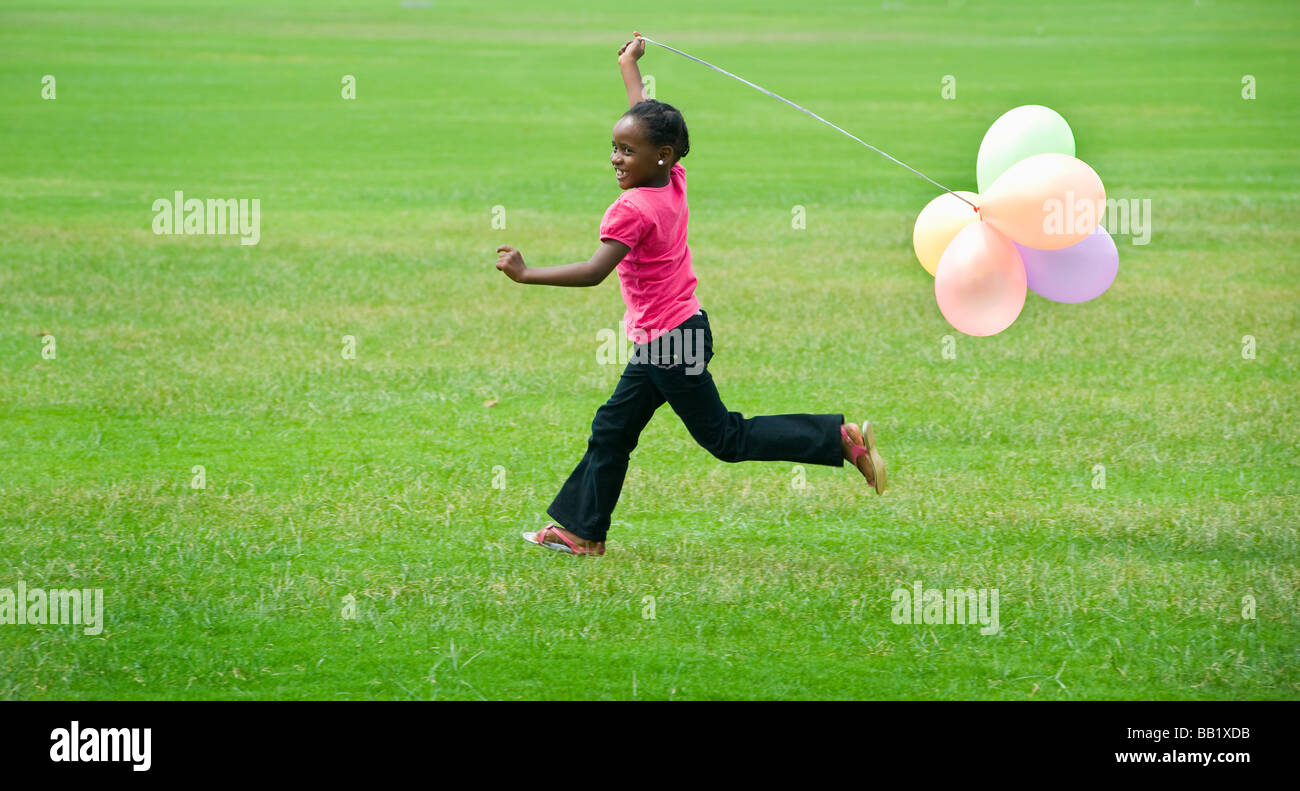Una giovane ragazza corre con palloncini su un campo in erba, Johannesburg, Sud Africa Foto Stock