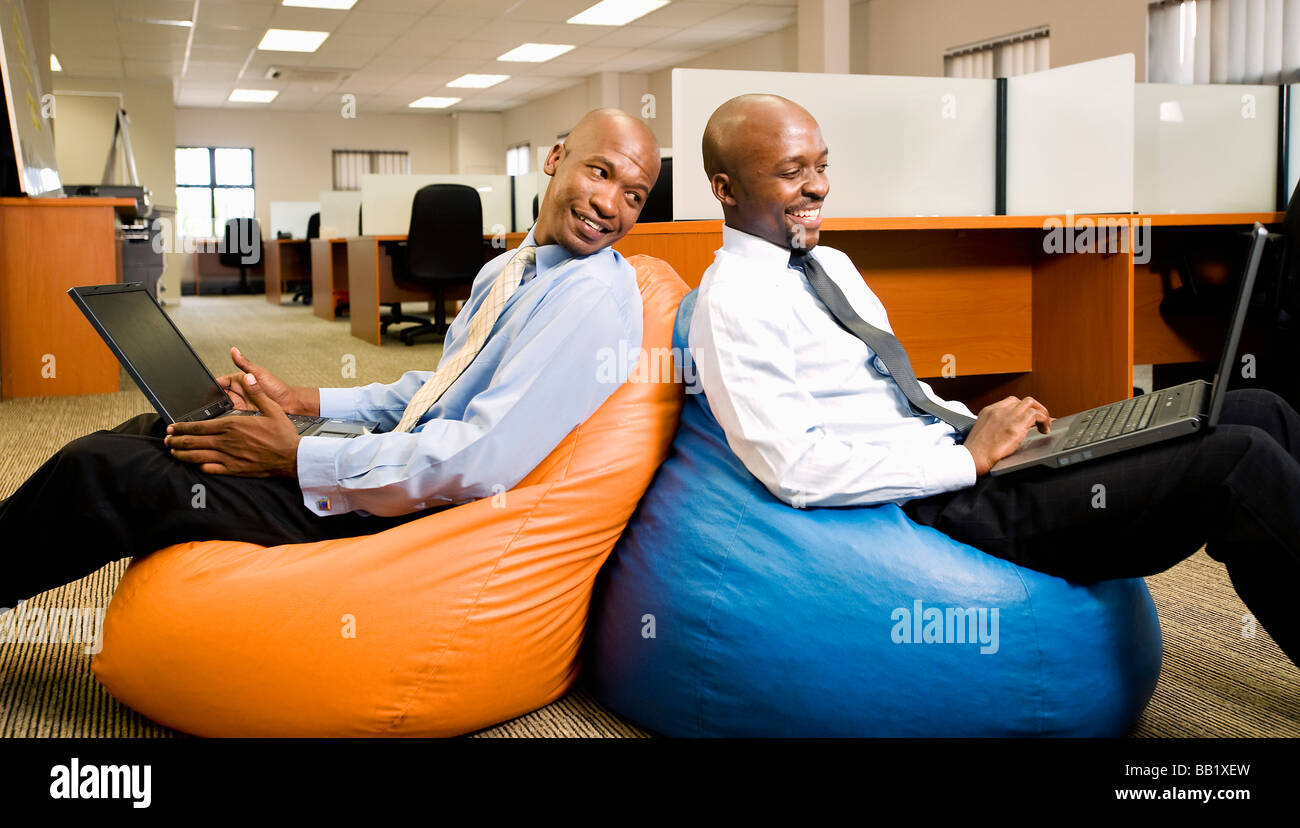 Due imprenditori confronta il lavoro sui laptop stando seduti su beanbags. Pretoria, Sud Africa Foto Stock