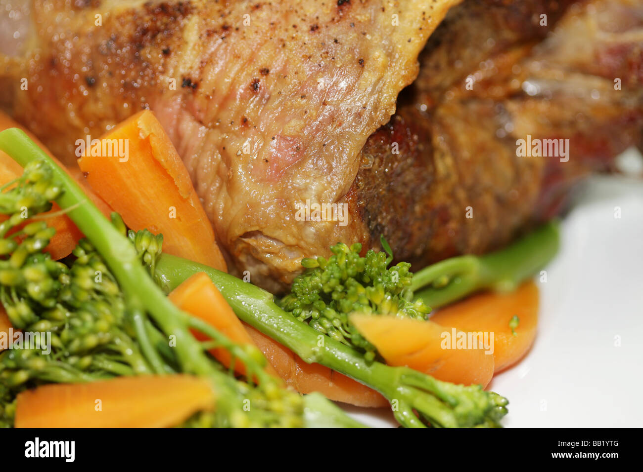 Tradizionale fresco cosciotto di agnello arrosto con verdure compresi i broccoli e carote isolata contro uno sfondo bianco con n. di persone Foto Stock