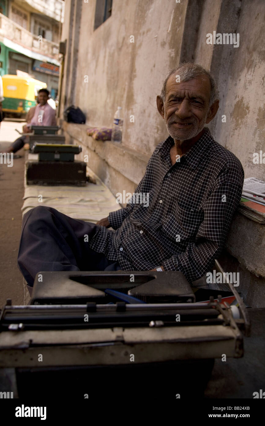 Un uomo si siede sulla strada lavorando su un typrewriter nel cuore della vecchia città di Ahmedabad, Gujarat. Foto Stock
