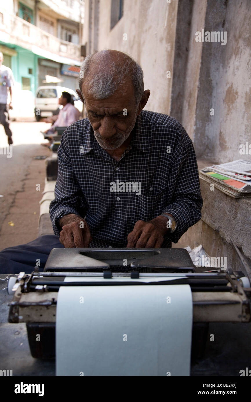 Un uomo si siede sulla strada lavorando su un typrewriter nel cuore della vecchia città di Ahmedabad, Gujarat. Foto Stock