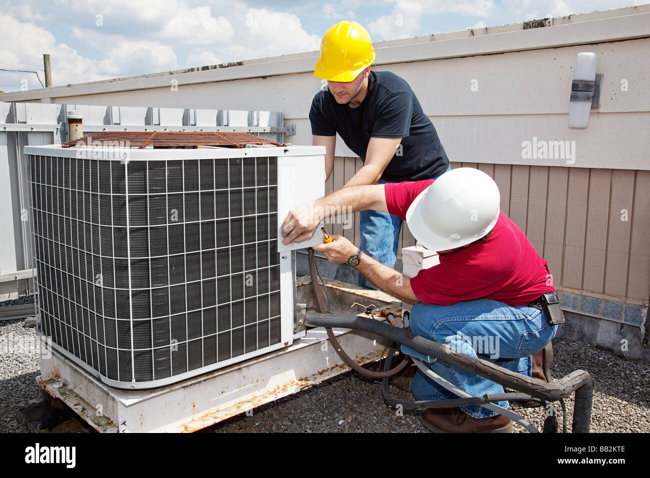 Due lavoratori sul tetto di un edificio lavorando sull'unità aria condizionata Foto Stock