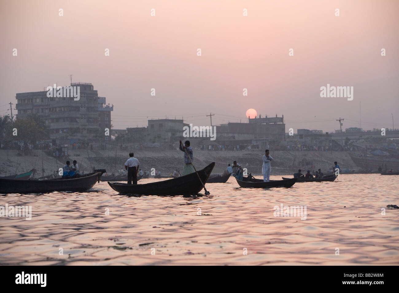 La vita quotidiana in Bangladesh; molte piccole barche a remi a lavorare al tramonto sul fiume Buriganga a Dhaka. Foto Stock