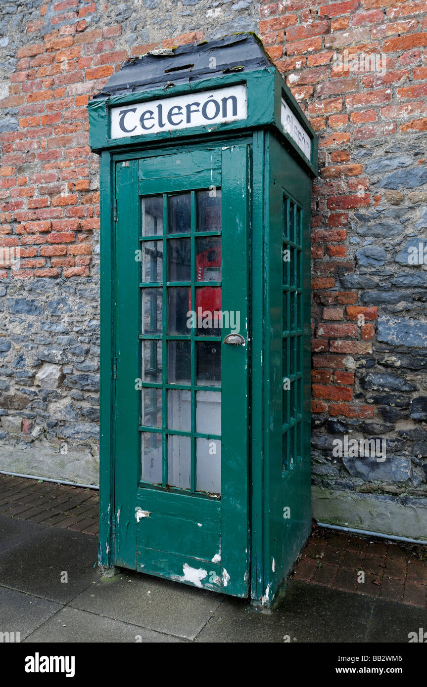 Irlandese tradizionale telefono verde box porta chiusa nella parte anteriore del rosso parete di mattoni vecchi inutilizzati disrepair in disuso la tecnologia obsoleta Foto Stock