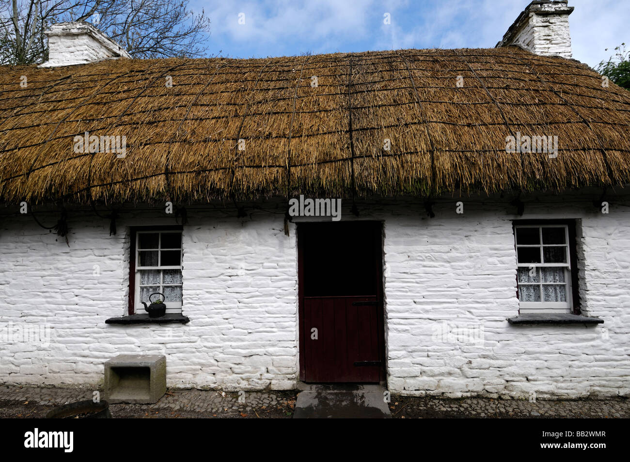 Tetto di Paglia cottage con open red porta in legno finestra bianca telaio verniciato bianco tradizionale casa di pietra blu cielo Irlanda Foto Stock