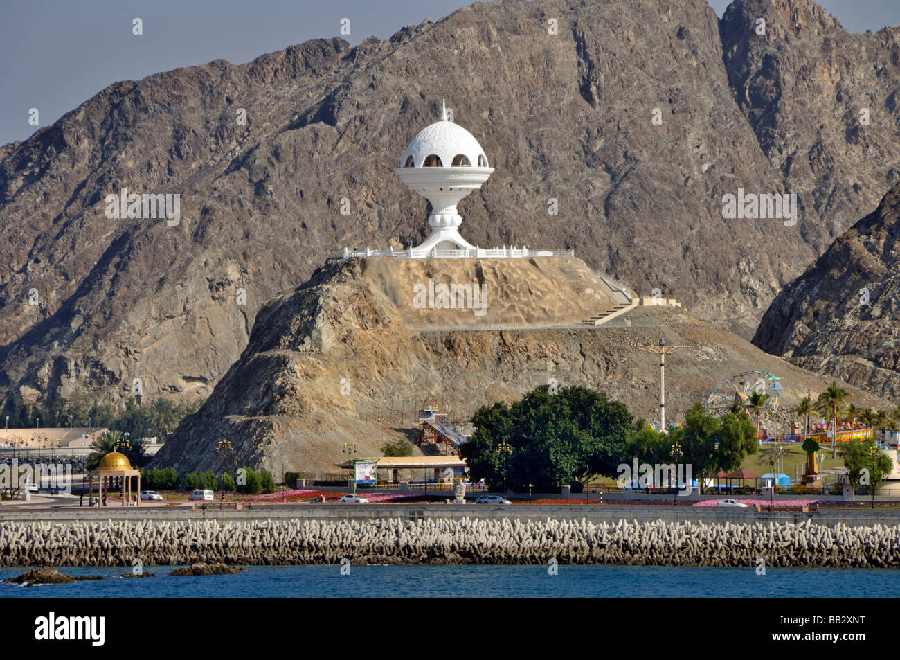 Il Muscat Oman waterfront con coste rocciose e Brucia incensi torre di guardia sulla collina sopra il parco locale & PARCO GIOCHI Foto Stock