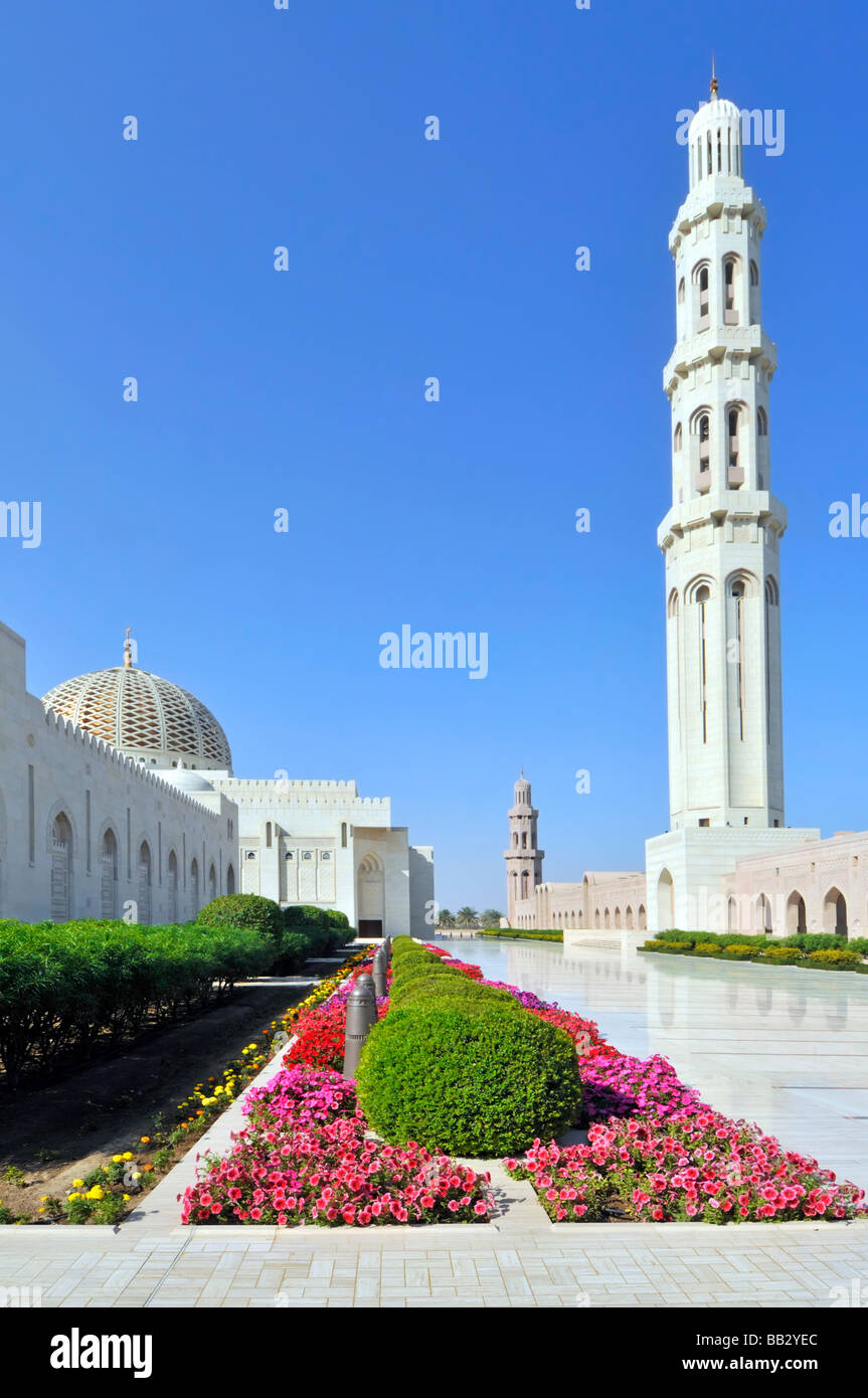 Minareto in splendida vista esterna degli edifici religiosi bianchi e dei fiori nella grande Moschea del Sultano Qaboos nel giorno del cielo blu di Mascate Oman, Medio Oriente Asia Foto Stock