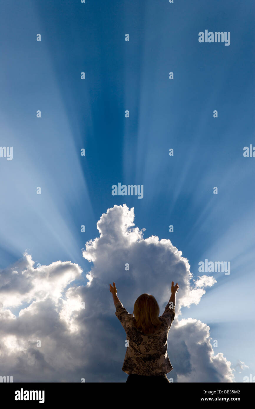 La donna si alza le mani in meraviglia come o crepuscolare Dio streak raggi passato cloud. Foto Stock