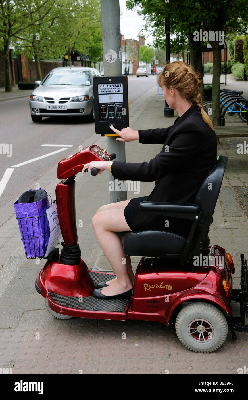 Femmina scooter di mobilità autista guida in città al centro di controllo del traffico del punto di incrocio premendo il pulsante per attraversare la strada Foto Stock