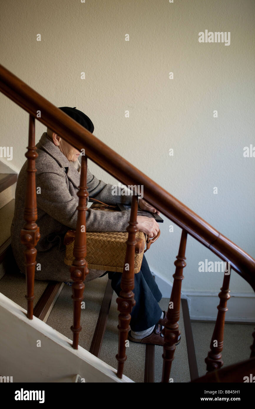 Senior seduta con una valigia su per le scale Foto Stock