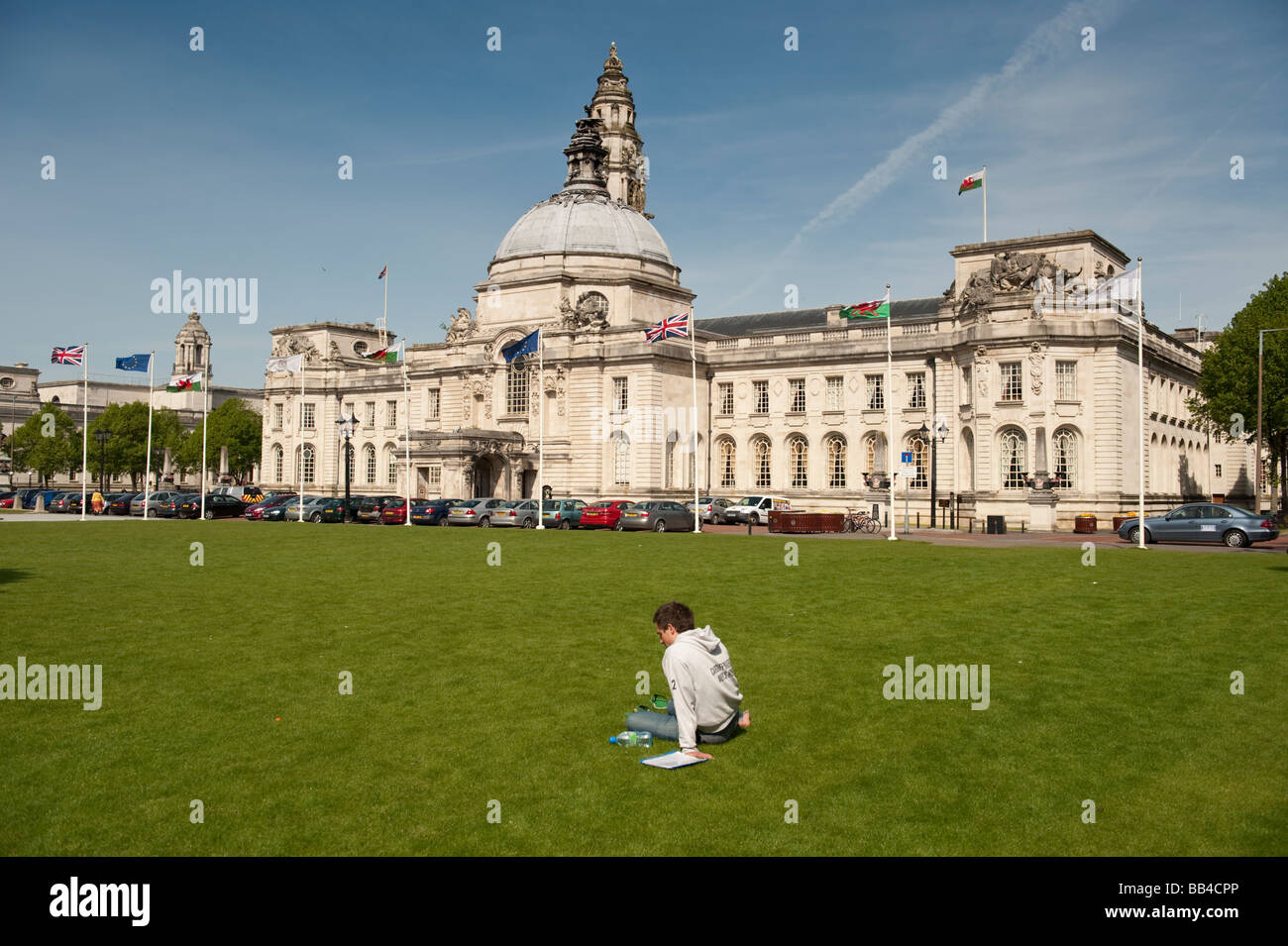 Giovane uomo seduto sull'erba al di fuori della citta' di Cardiff county hall e il centro civico Wales UK Foto Stock