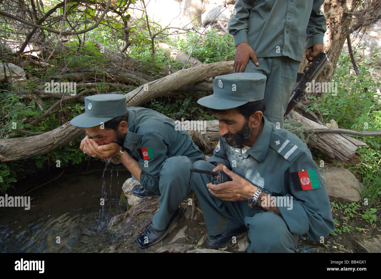 Poliziotti afghani vasca da bagno le loro facce e bere da una molla considerata avere proprietà curative, durante una pattuglia in Foto Stock
