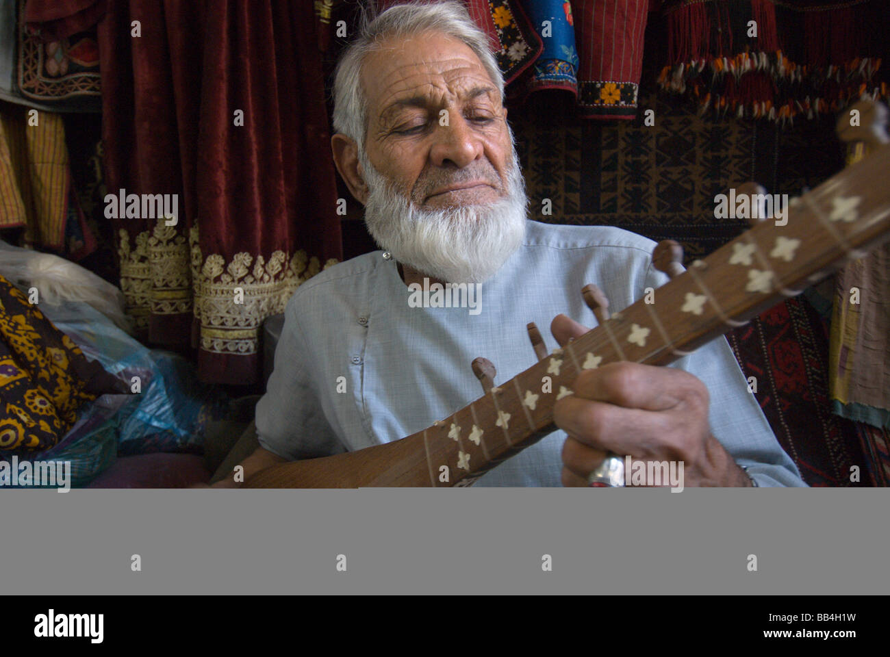 Un negoziante in un negozio vicino alla Moschea del Venerdì, Haji Sultan Hamidi, riproduce Tanboor, un classico strumento a corda della centrale come Foto Stock