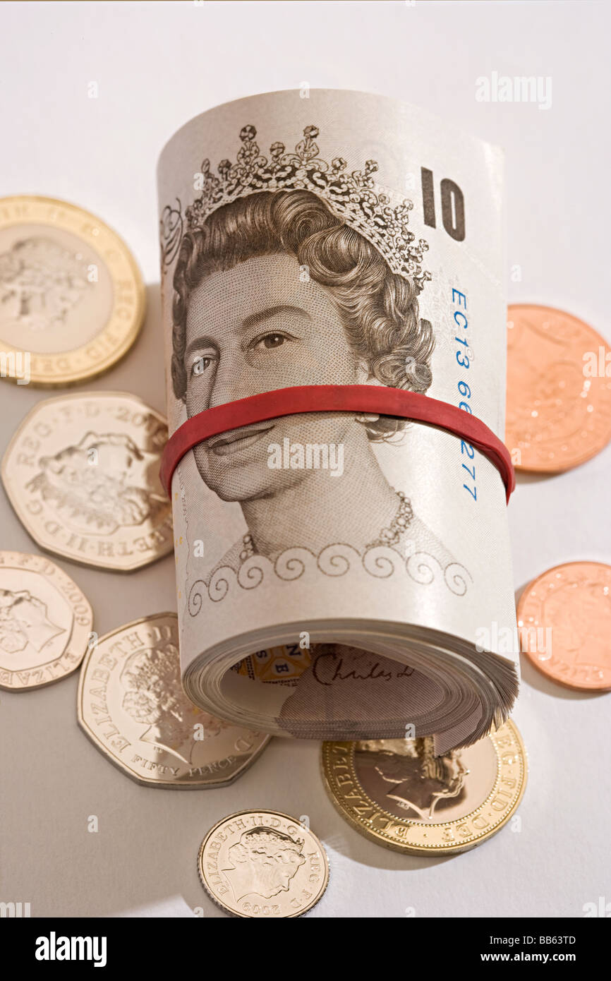Nuovo e inutilizzato rotolo di sterline inglesi mint dieci pound banconote arrotolate giacente su di coniare monete inutilizzate. Foto Stock