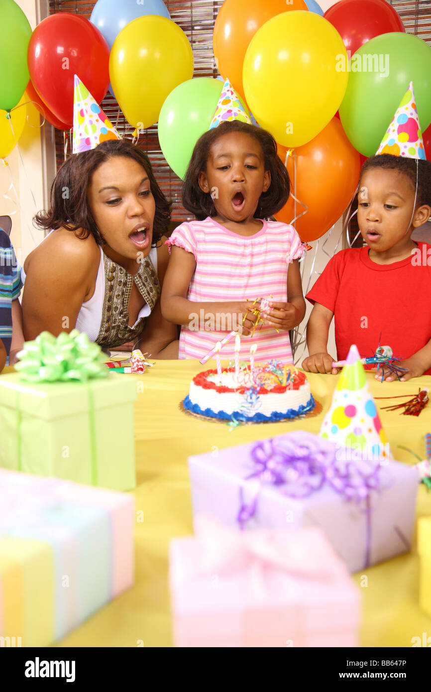 Giovane ragazza che spegne le candeline sulla torta del compleanno con aiuto dalla madre e fratello Foto Stock