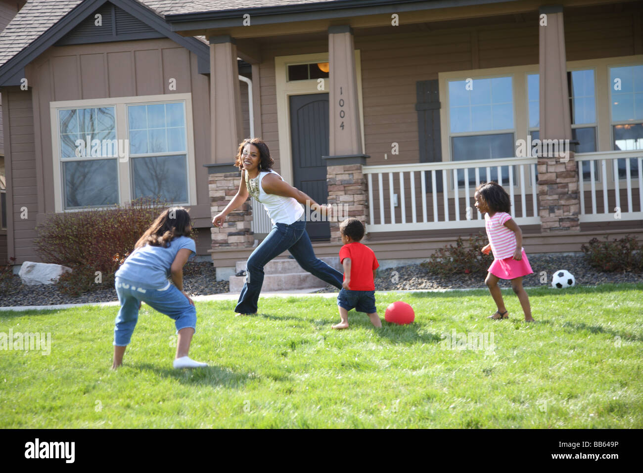 Madre e bambini correre e giocare nel cortile anteriore Foto Stock