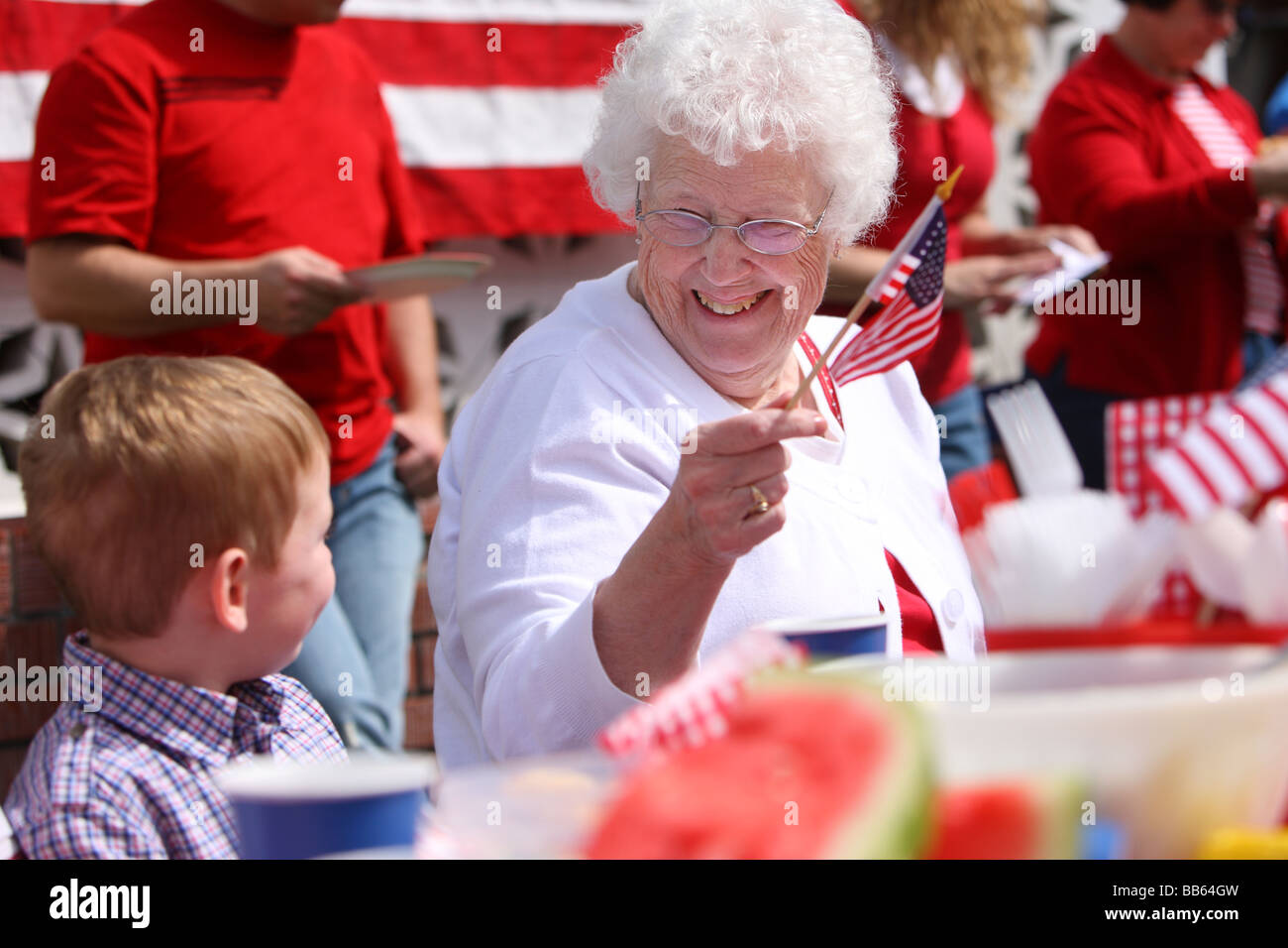 Donna anziana in famiglia barbecue sventola bandiera americana Foto Stock