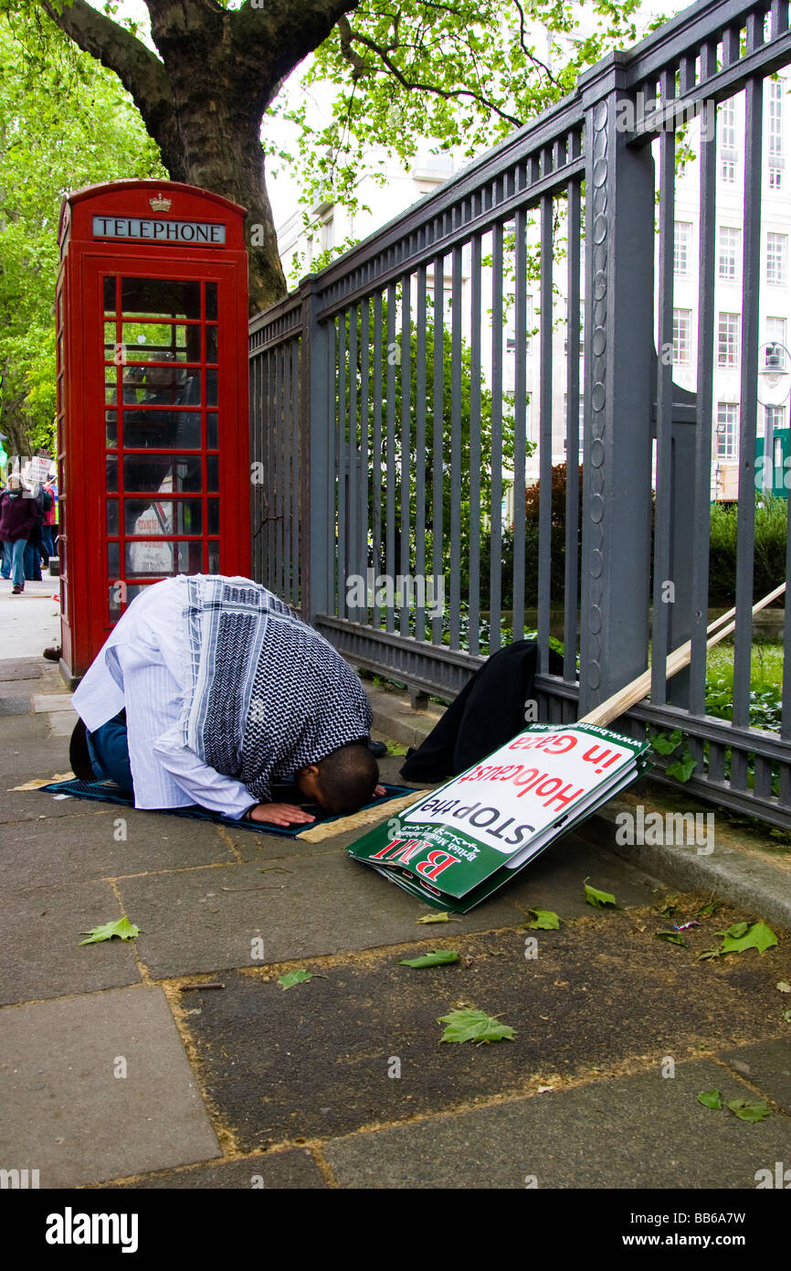 Prima di iniziare una protesta circa la situazione in corso nella Striscia di Gaza un uomo musulmano prega alla Mecca su una strada di Londra. Foto Stock