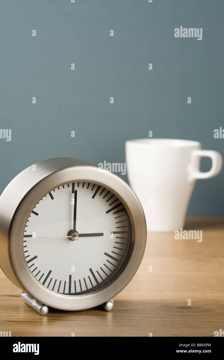 Un orologio che mostra tre o di un orologio con una tazza di tè dietro Foto Stock