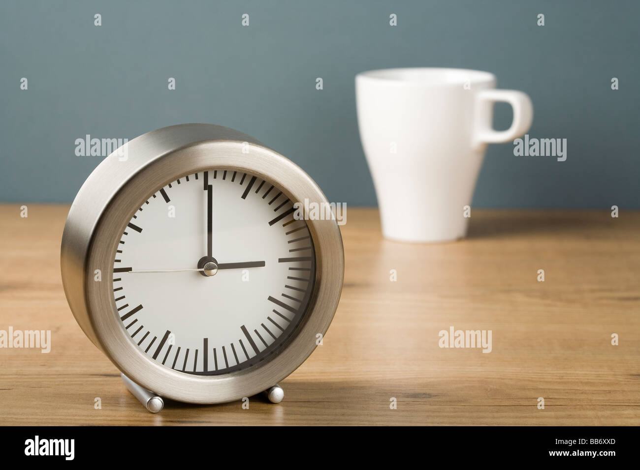 Un orologio che mostra tre o di un orologio con una tazza di tè dietro Foto Stock