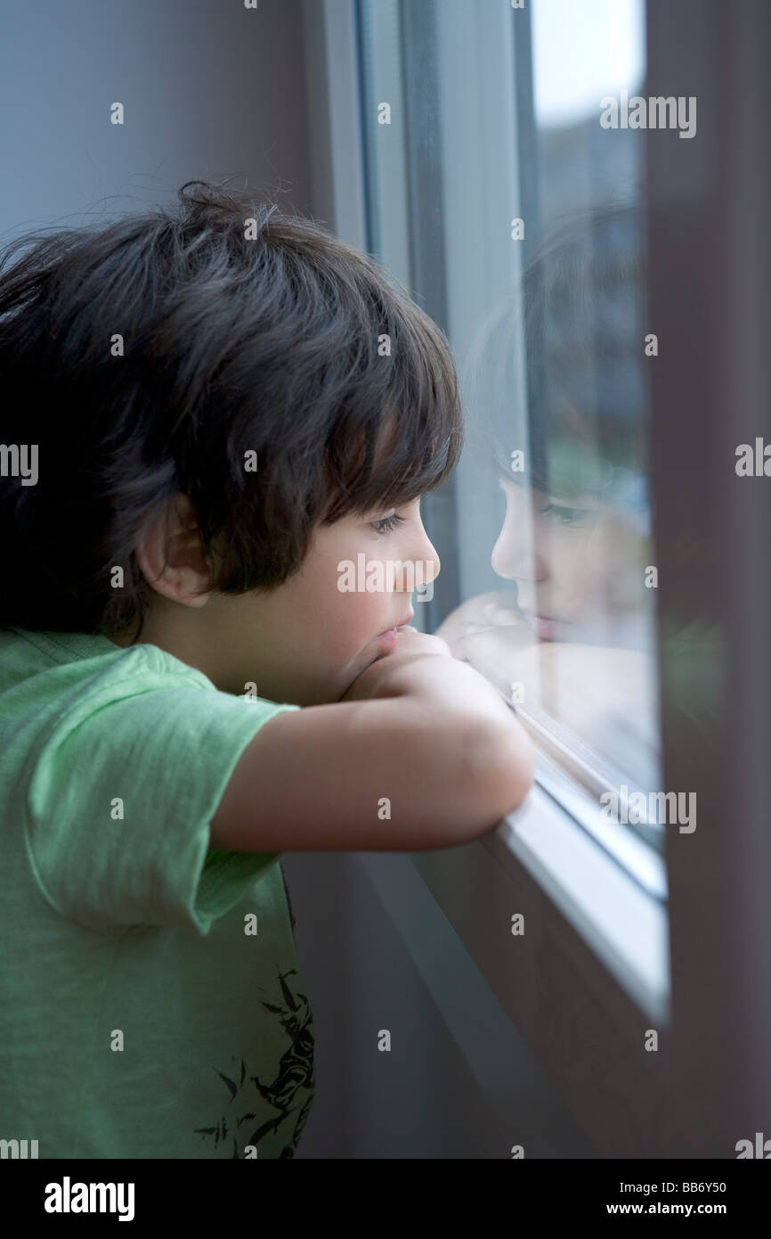 Lonely little boy guardando fuori della finestra Foto Stock