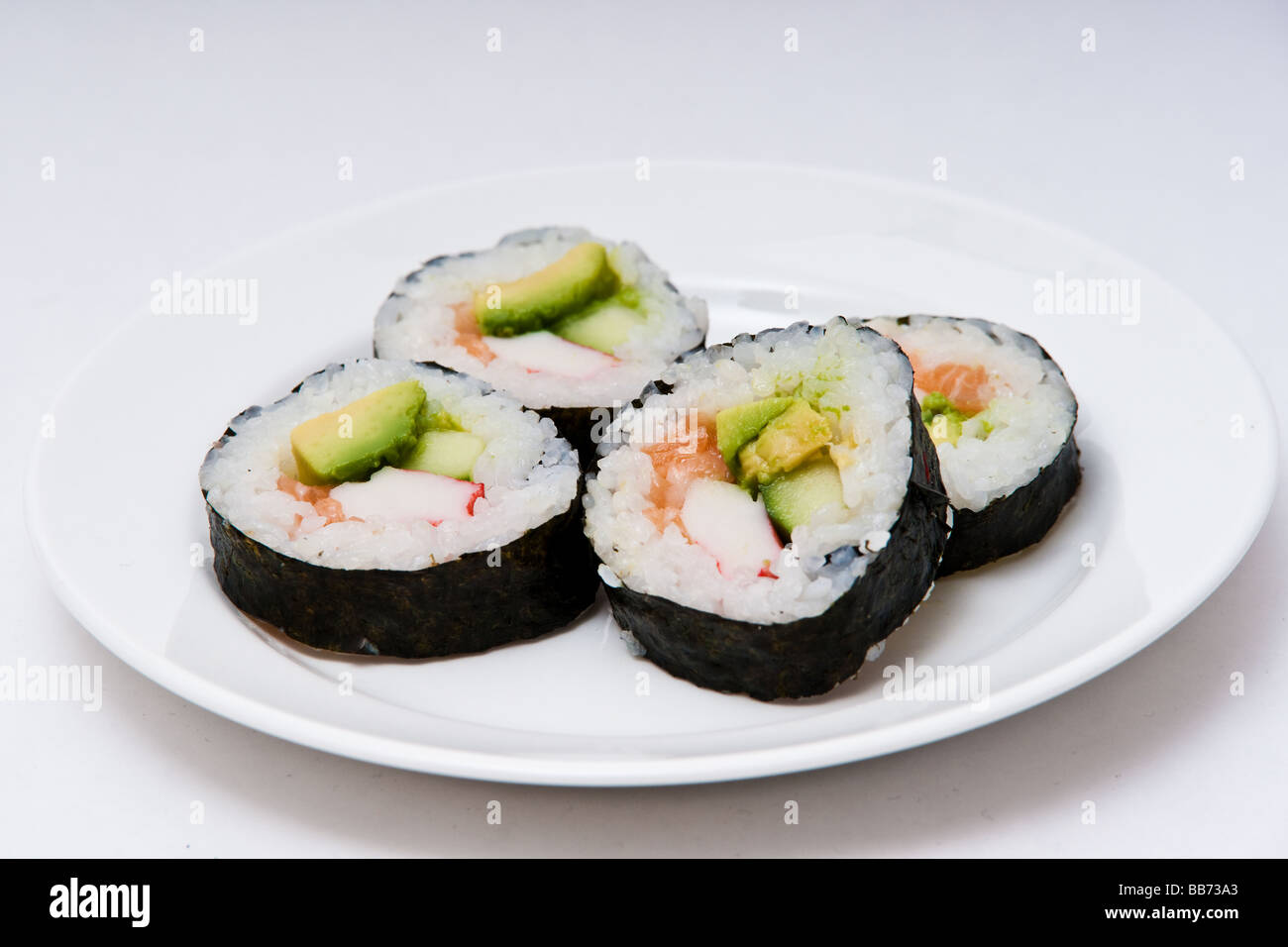 Una piastra bianca con quattro maki sushi rotoli contenenti il riso, salmone, avocado e cetrioli avvolto in nori, alghe. Foto Stock