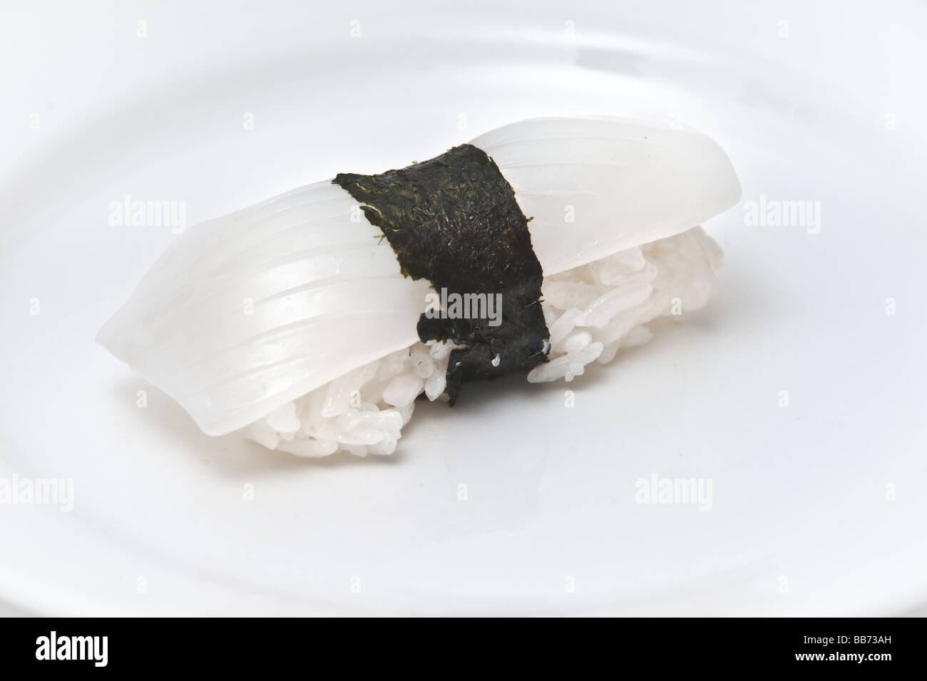 Una piastra bianca con un calamaro pezzo di sushi, sashimi nigiri, su un letto di riso e avvolti insieme a Nori, alghe marine Foto Stock